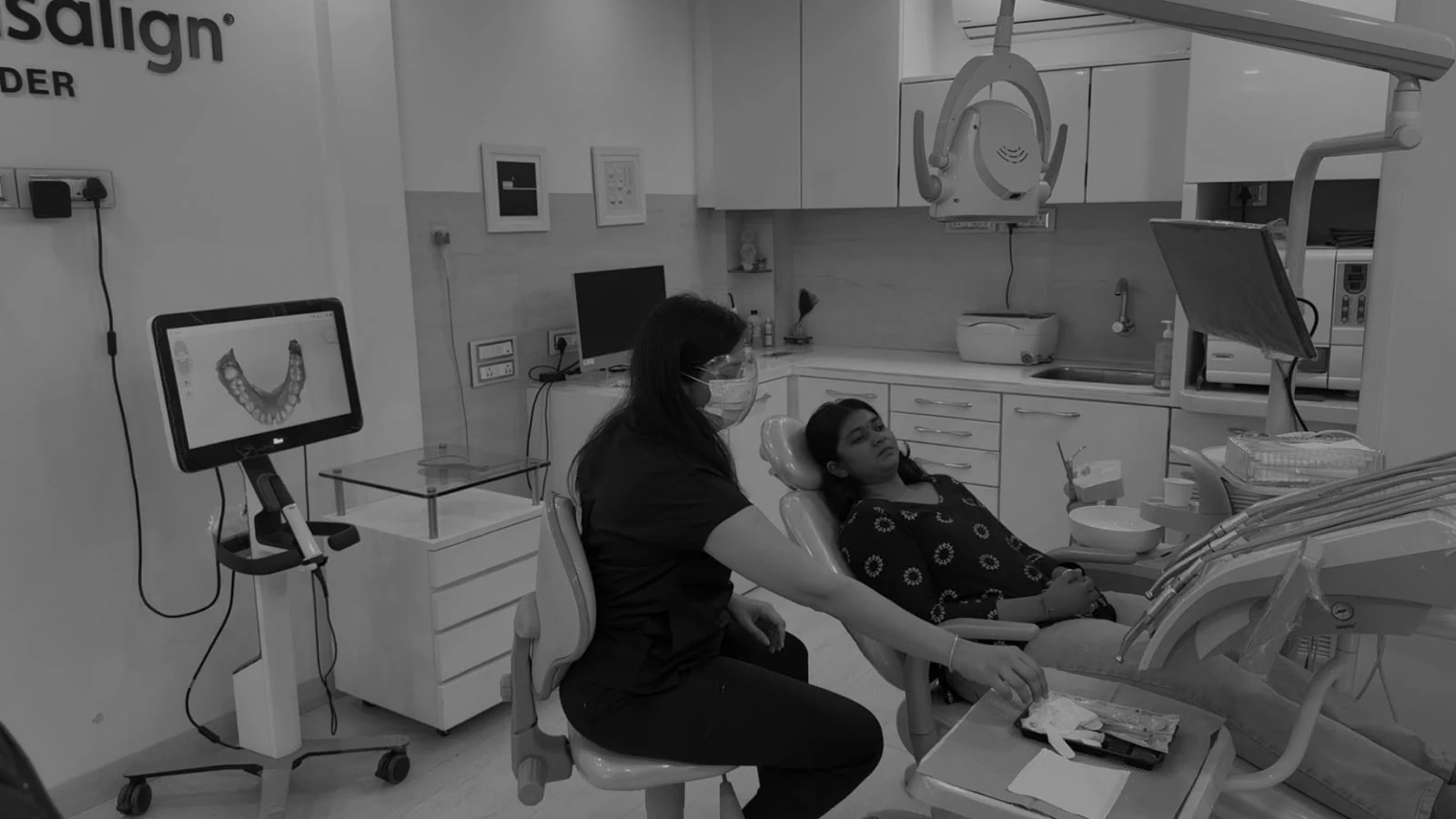 Dr. Feril Mehta seated beside a patient during a 3D smile scan, with the clinic scanner display visible